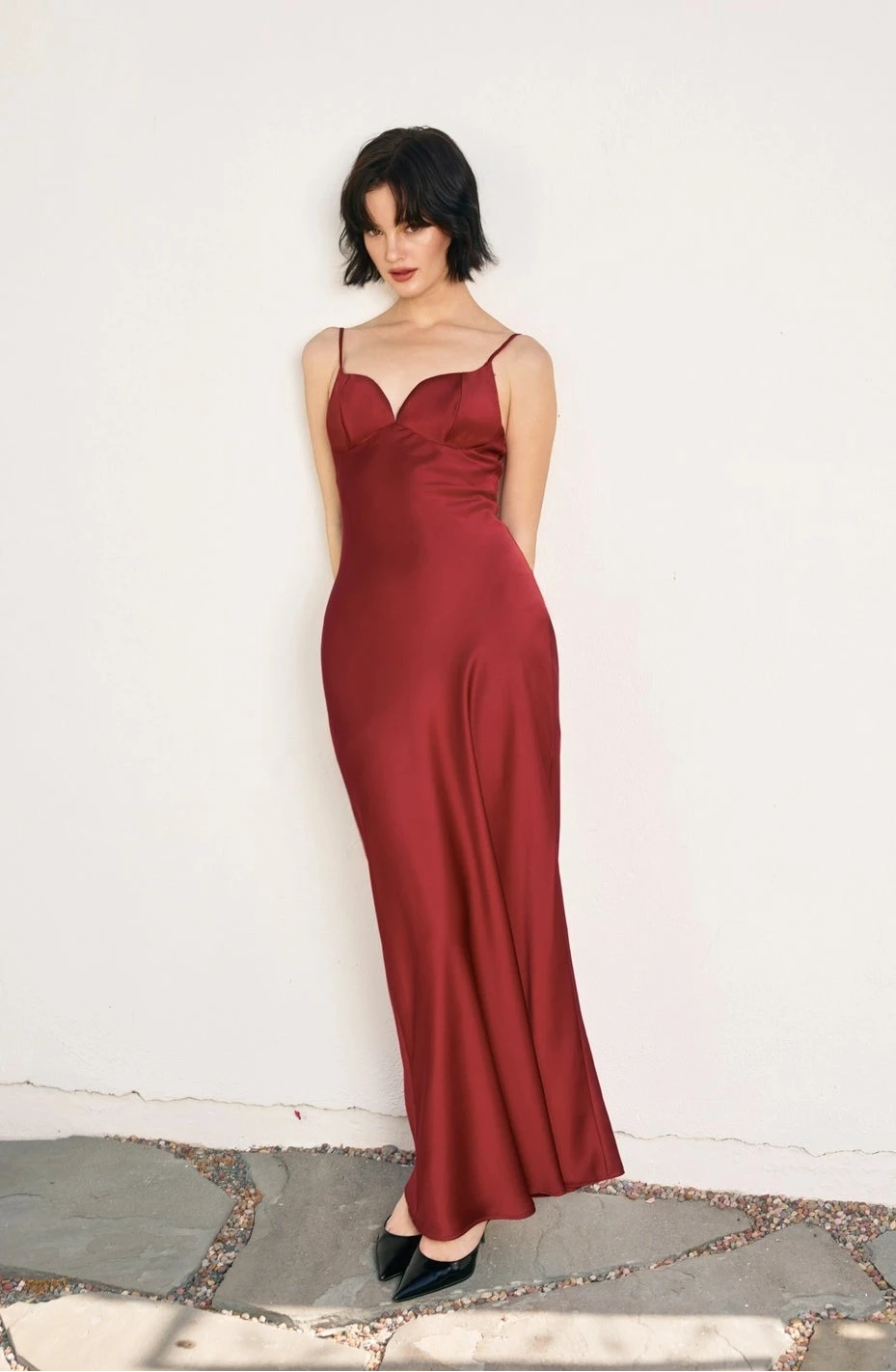 Woman wearing a red evening gown against a white wall.