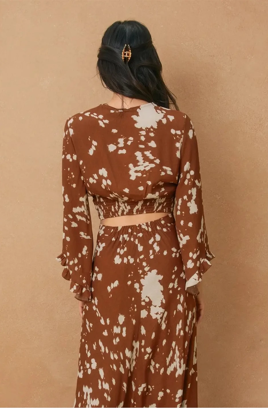 Woman wearing a brown and white patterned dress against a beige background