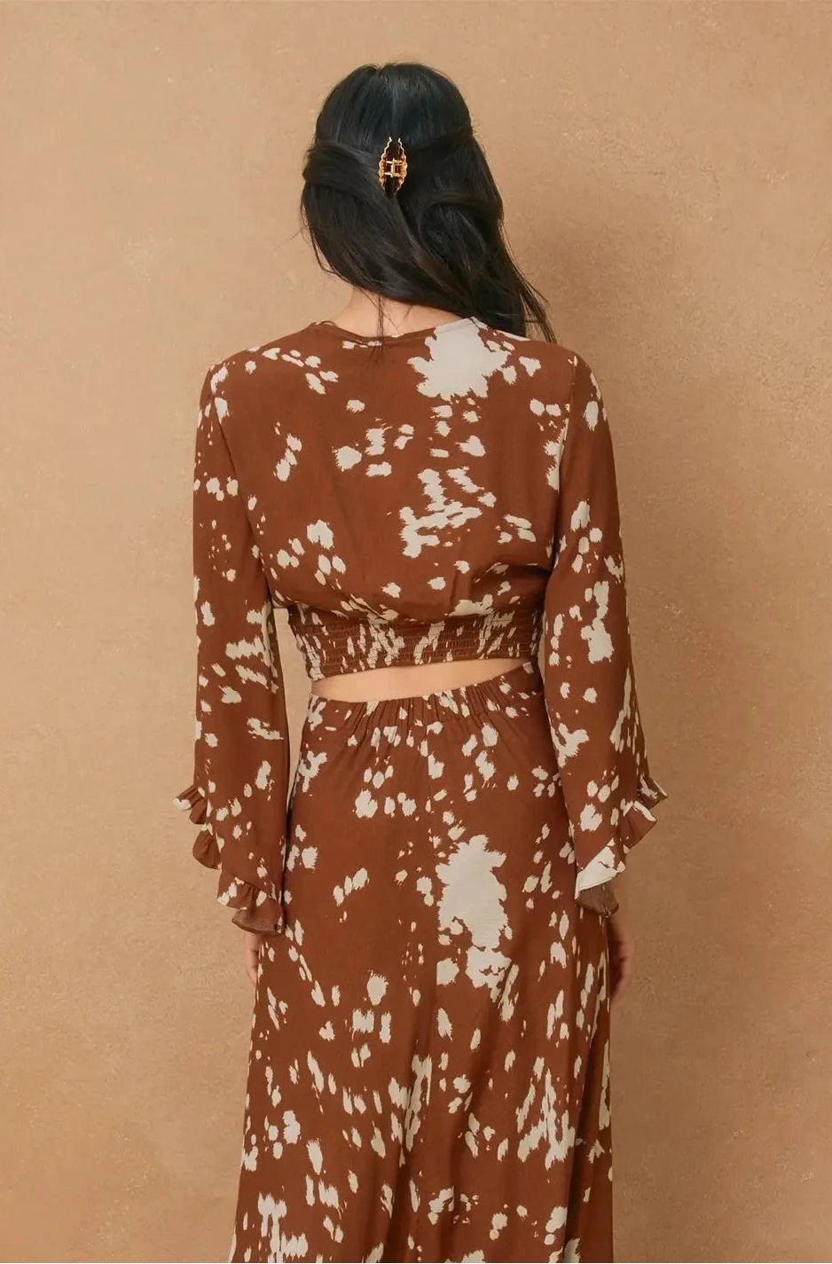 Woman wearing a brown and white patterned dress against a beige background