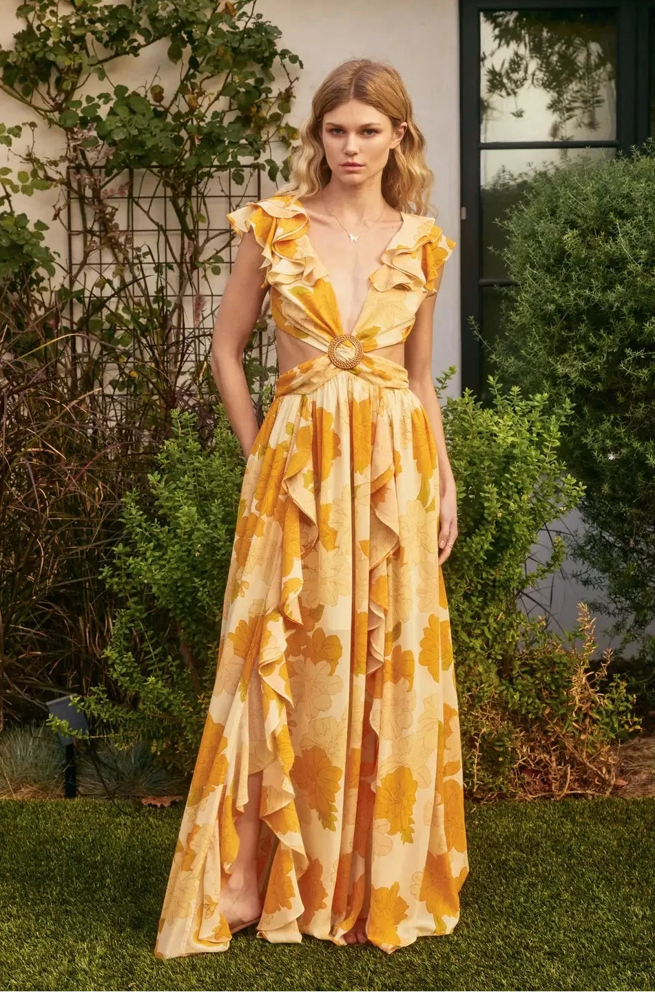 Woman wearing a yellow floral dress standing outdoors with greenery in the background