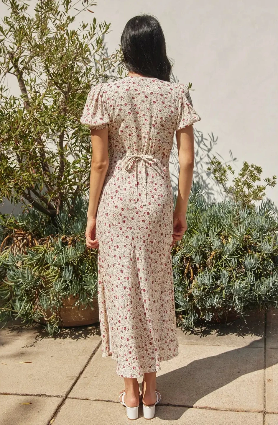 Woman wearing a floral dress standing outdoors with greenery in the background