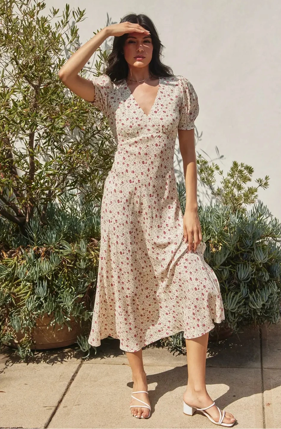 Woman wearing a floral dress standing outdoors with plants in the background