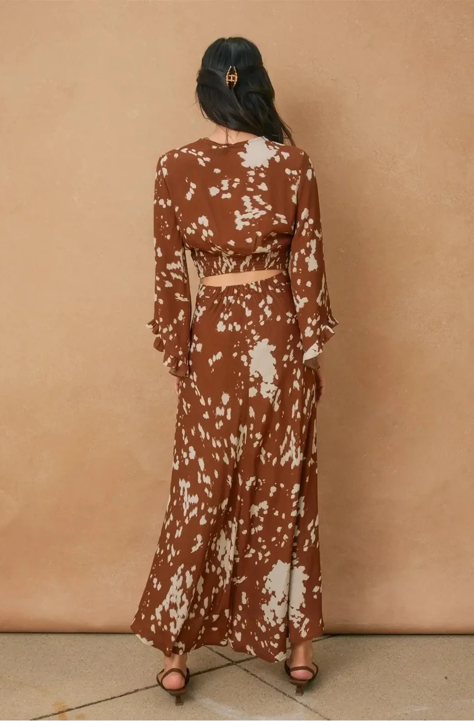 Woman wearing a brown and white patterned outfit against a beige wall.